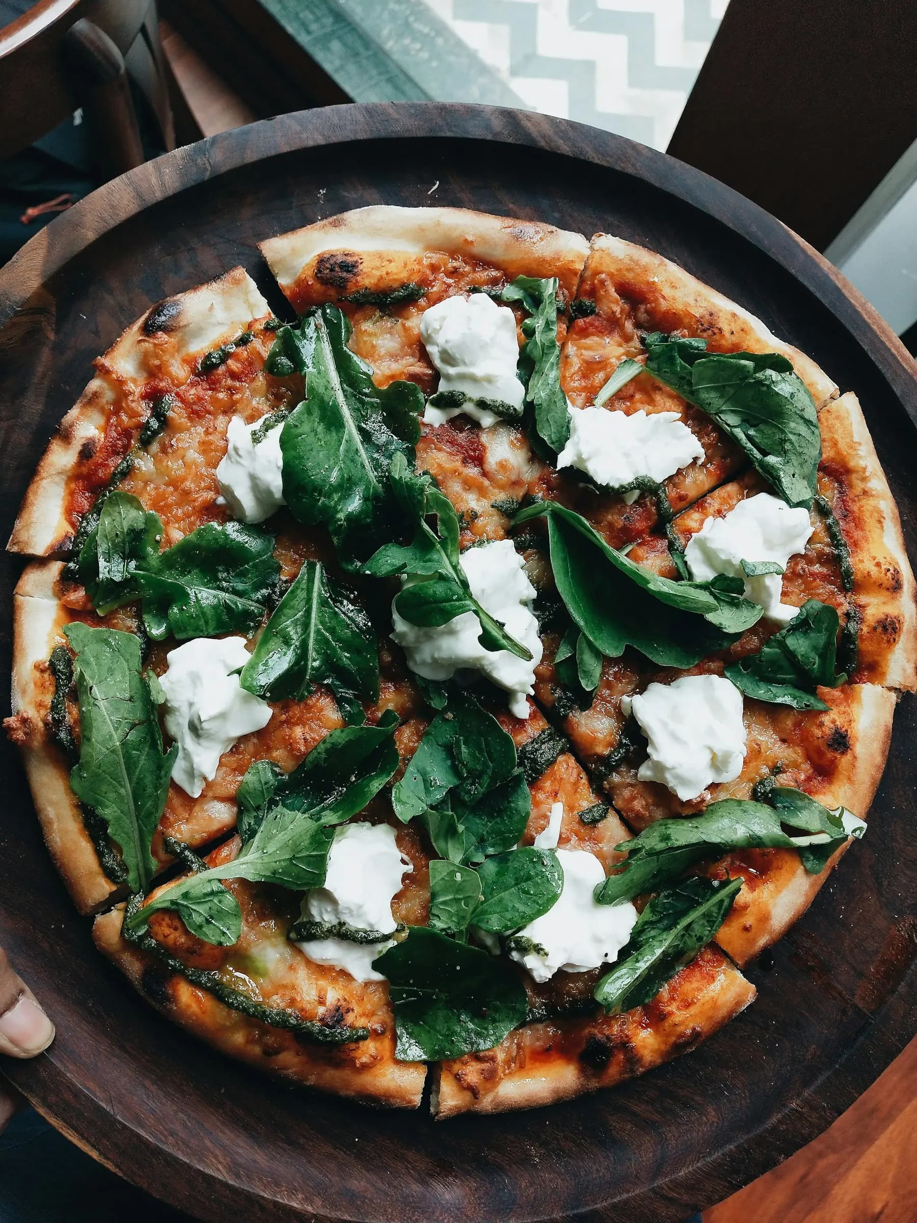 Une pizza roquette, mozzarella et pesto sur une planche en bois