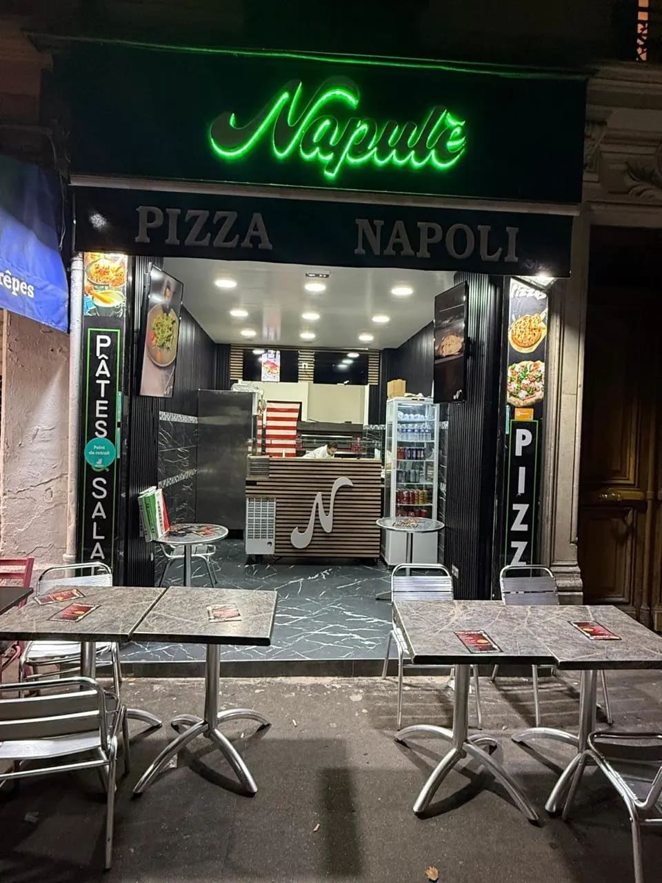 La devanture de L'art Napulè le soir, enseigne néon verte au 4 boulevard de Clichy à Paris, avec les tables en terrasse